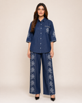 A woman modeling a matching navy blue two-piece set consisting of a short-sleeve button-up shirt and wide-leg trousers, both featuring white floral embroidery.
