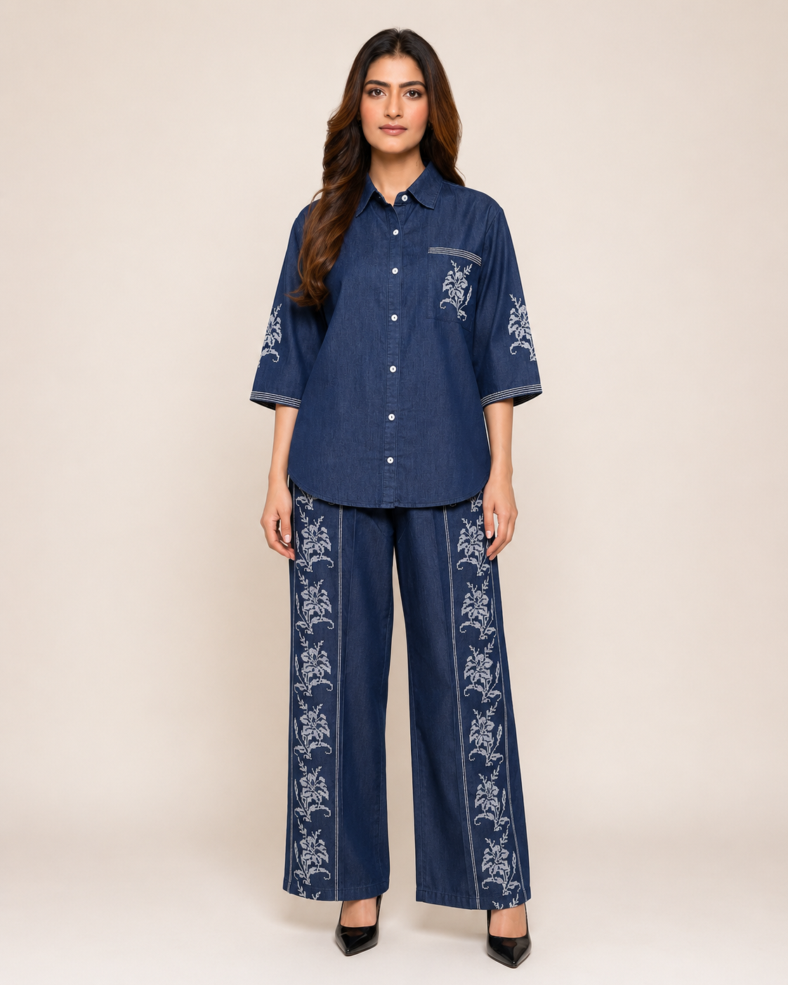A woman modeling a matching navy blue two-piece set consisting of a short-sleeve button-up shirt and wide-leg trousers, both featuring white floral embroidery.
