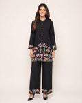 A woman modeling a black two-piece kurta and trouser set with colorful embroidered animal motifs around the hem and cuffs, photographed against a plain light beige studio background.