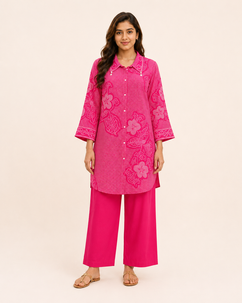 A woman modeling a bright pink kurta set with floral embroidery, consisting of a long-sleeve button-up tunic and matching wide-leg pants, against a solid light beige background.