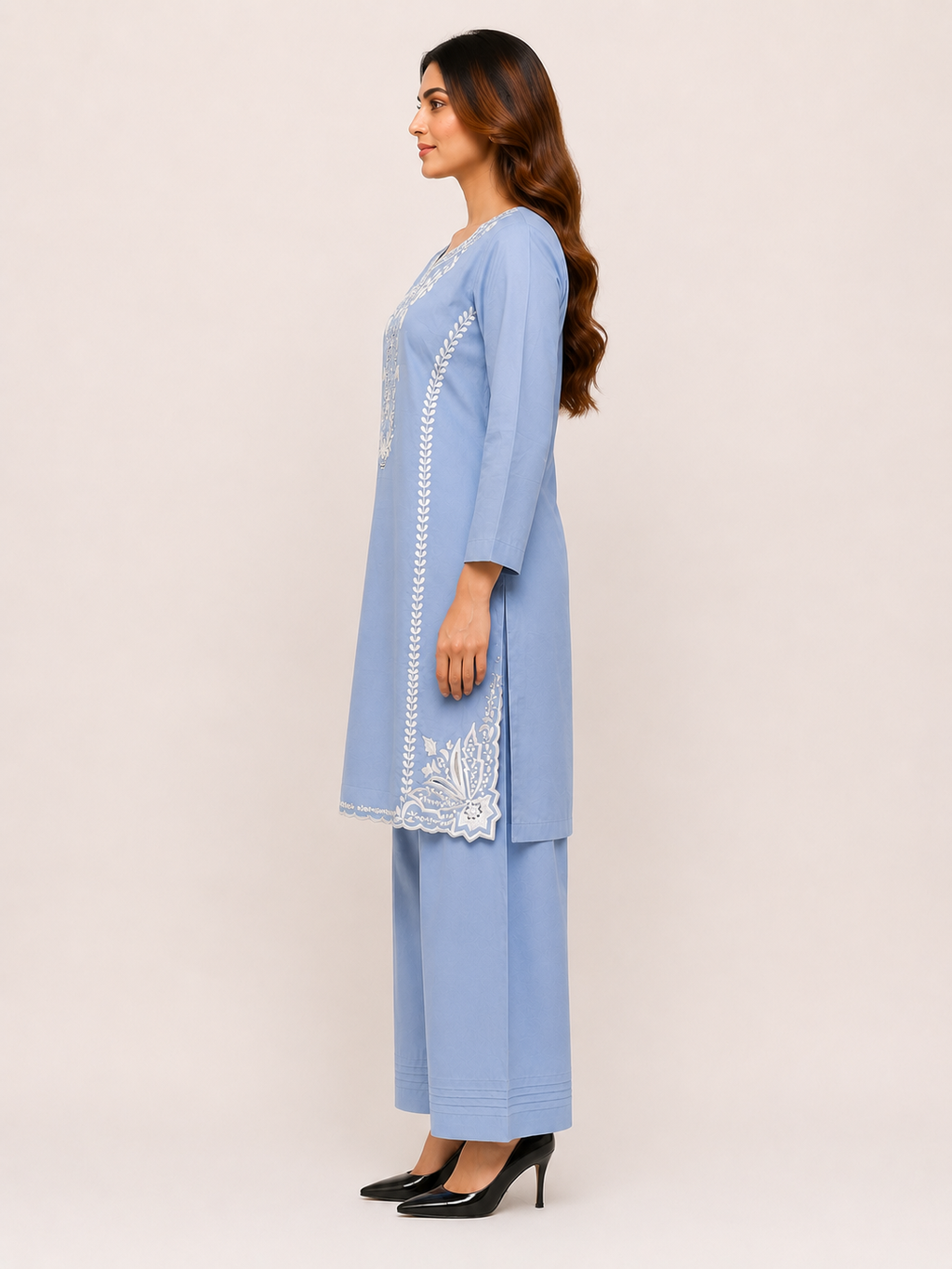A woman modeling a light blue three-piece kurta set with white embroidery, shown in profile against a plain beige studio background.