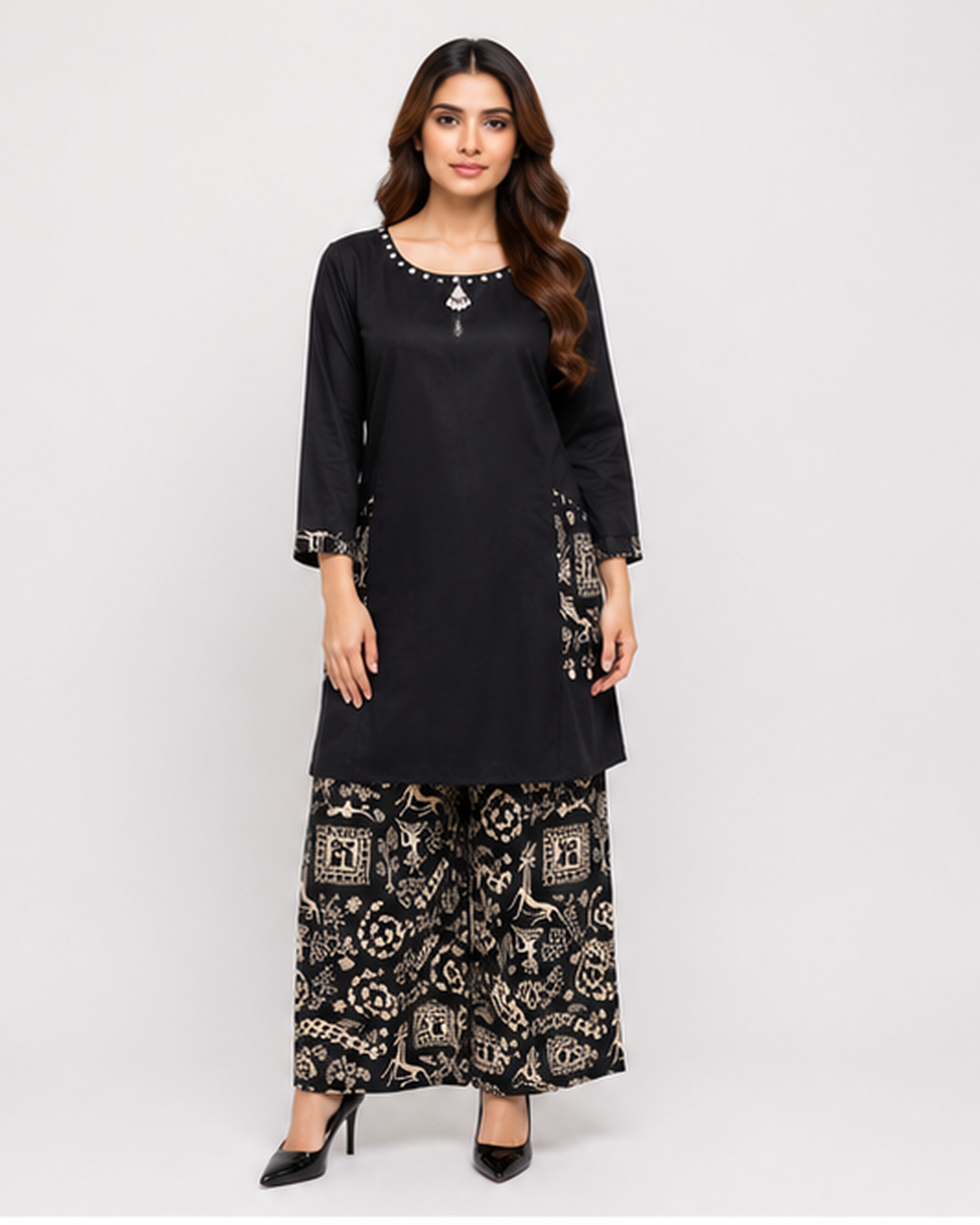A woman modeling a black kurta with silver embellishments and wide-leg black pants featuring a beige and gold block-print pattern, set against a plain light gray background.